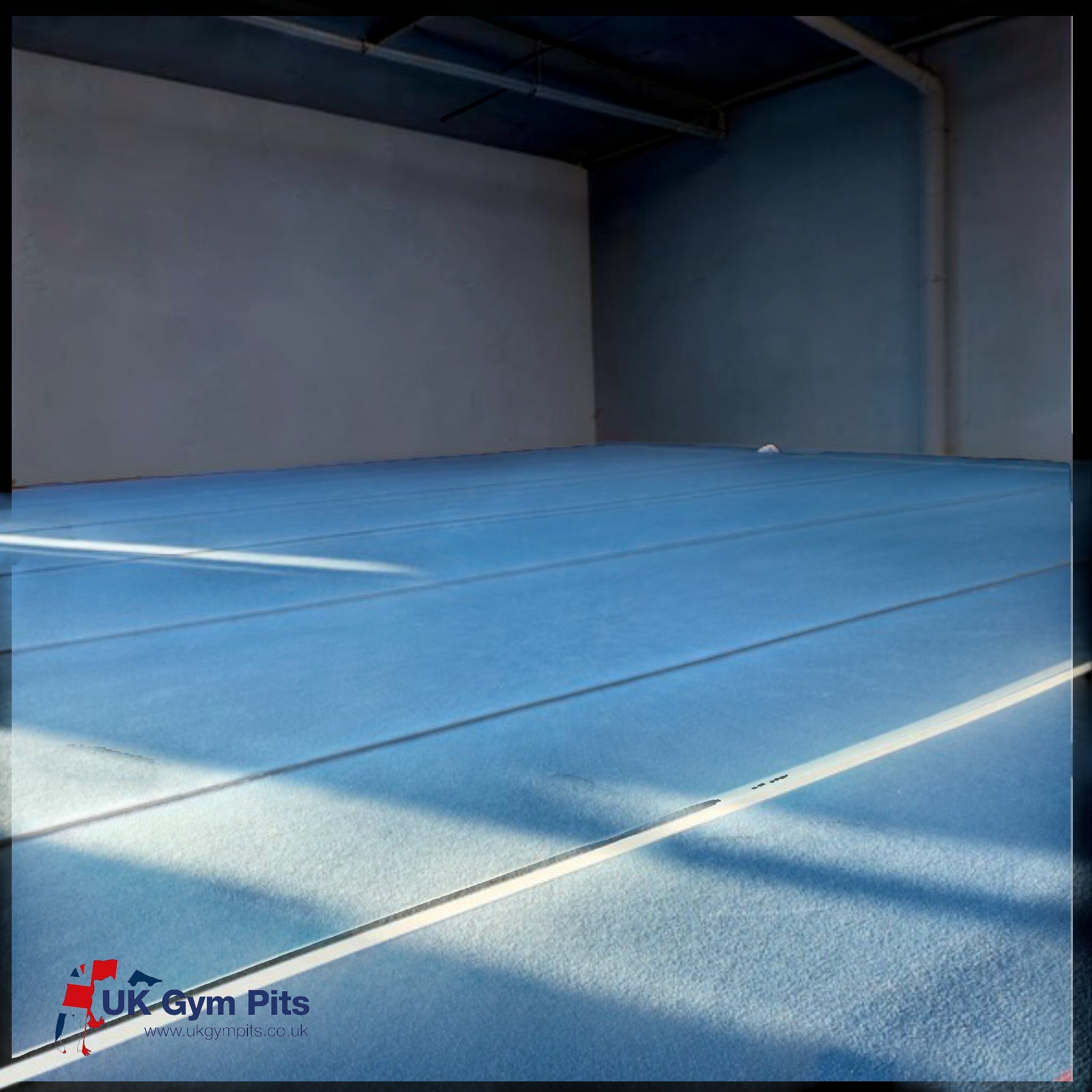 UK Gym Pits blue gymnastics sprung floor covering a large indoor training area with carpet mat rolls.