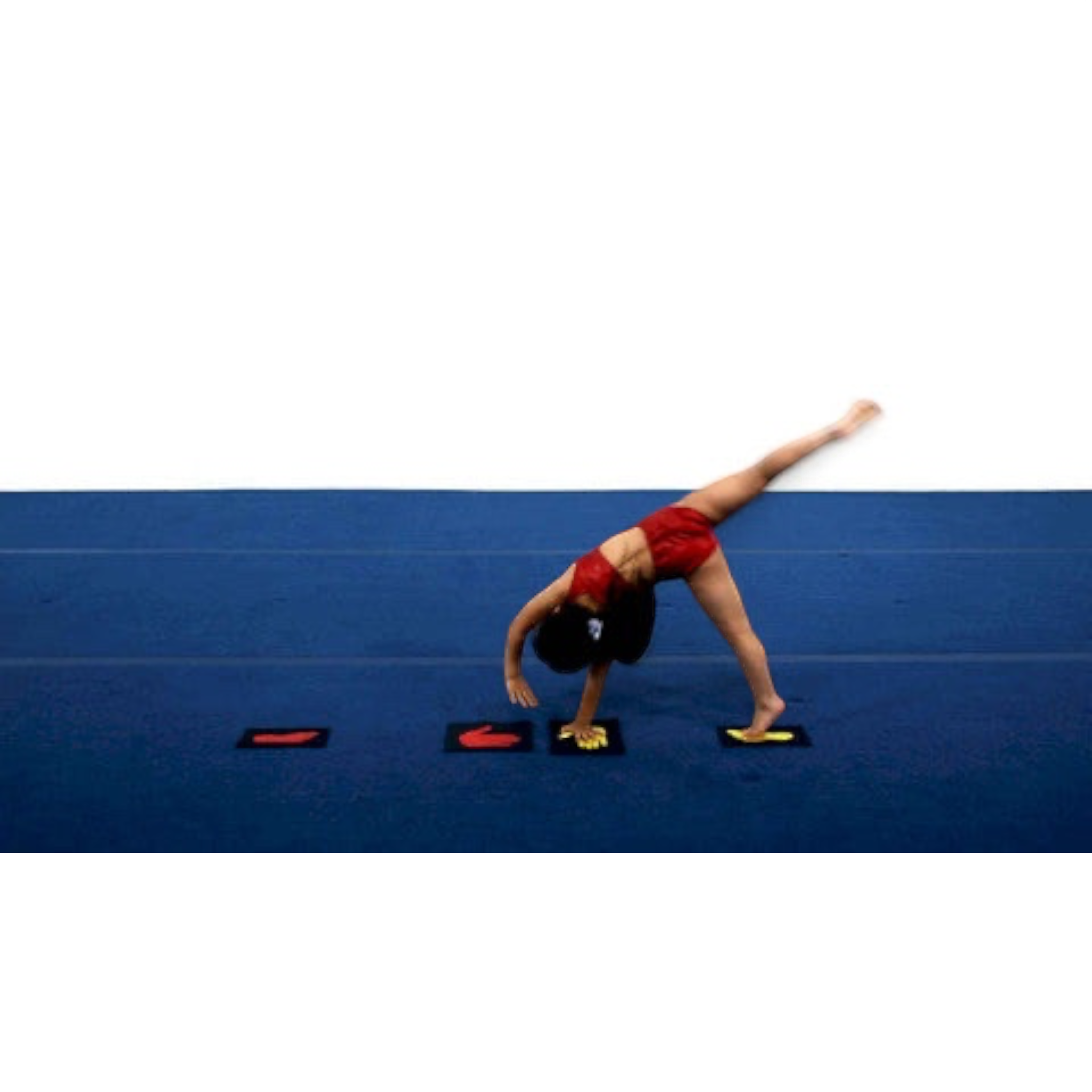 A young gymnast practicing a cartwheel on a blue mat using UK Gym Pits red and yellow hand and foot markers.