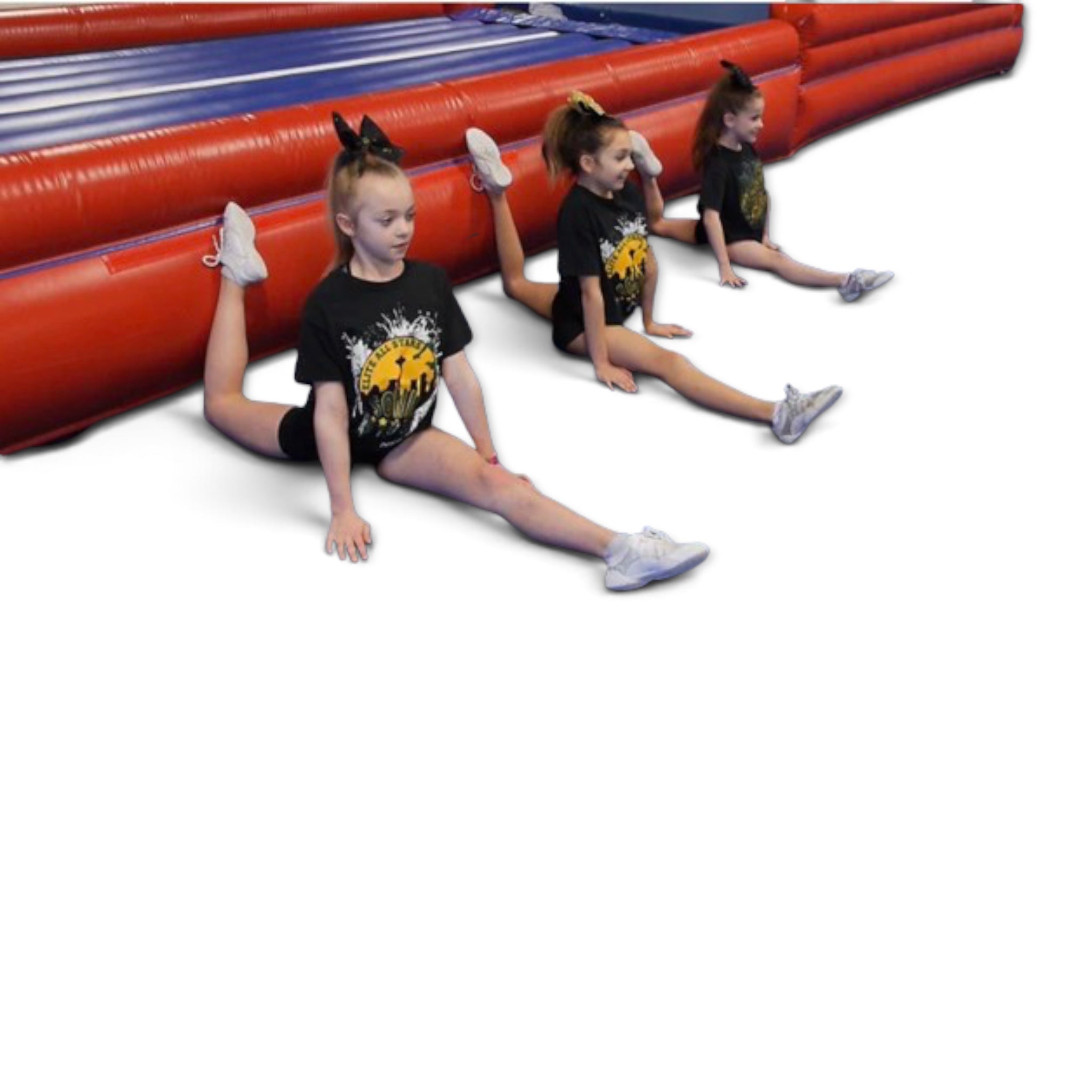 Three young gymnasts in black t-shirts performing splits in front of a red and blue UK Gym Pits inflatable air trak