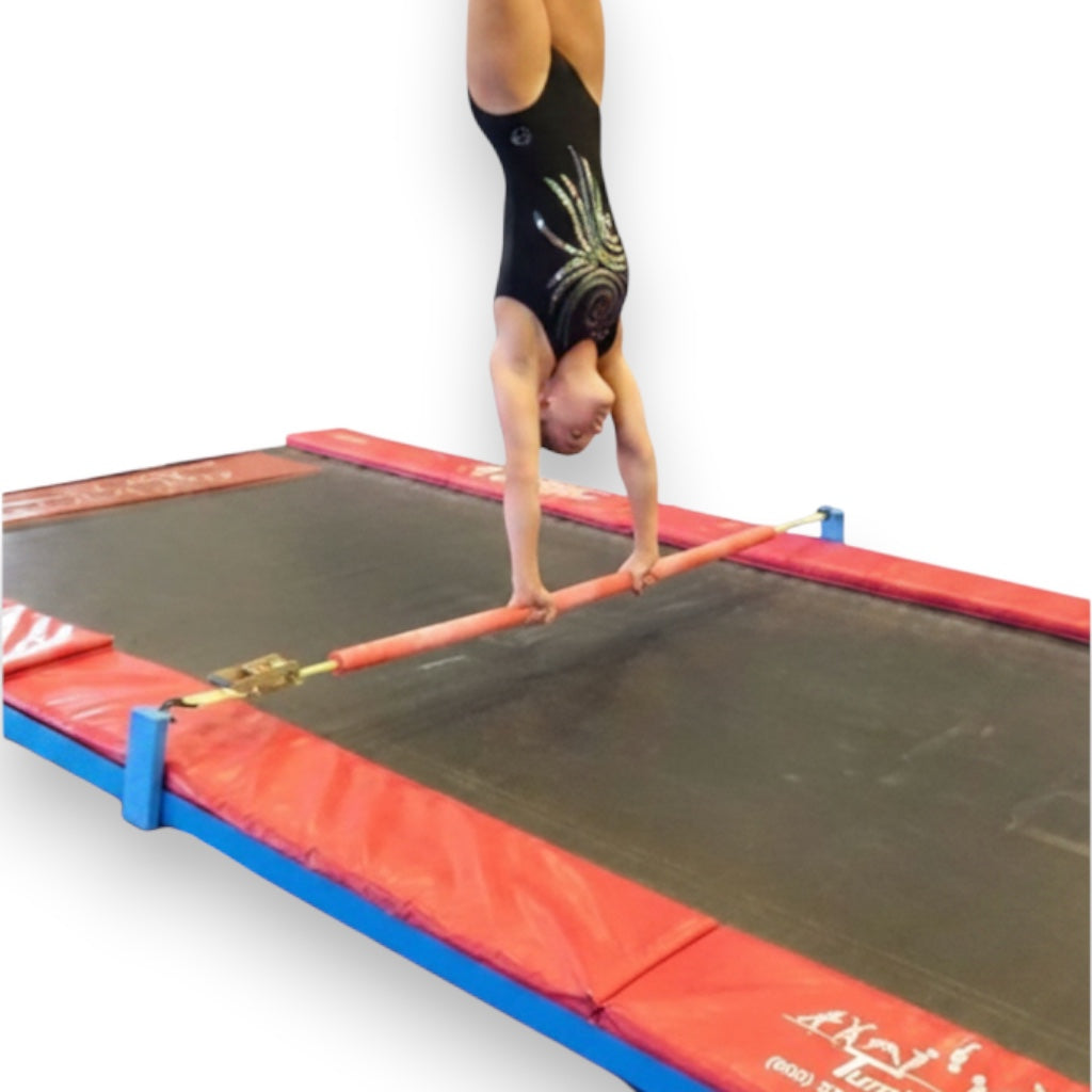 UK Gym Pits Quick Flex bar with foam padding attached to a Tumbl Trak, used by a gymnast in a handstand position.