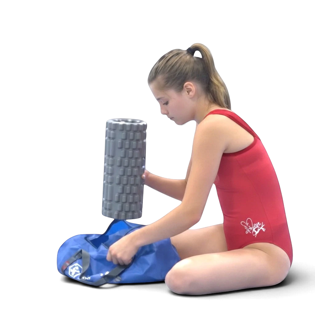 A young gymnast in a red leotard packing a grey foam roller into a blue UK Gym Pits athlete recovery kit travel bag.