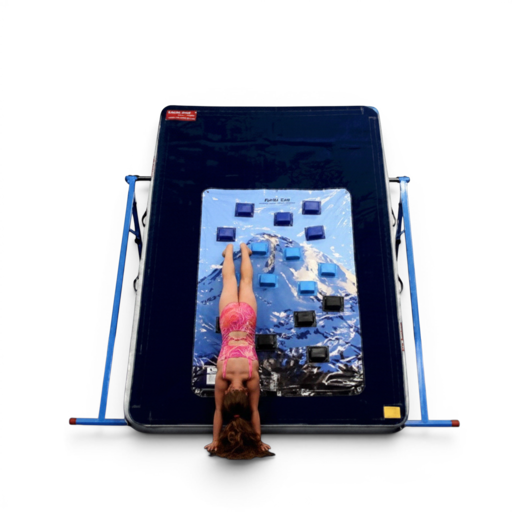 UK Gym Pits climbing wall overlay with blue foam holds attached to a mat, featuring a child performing a handstand.