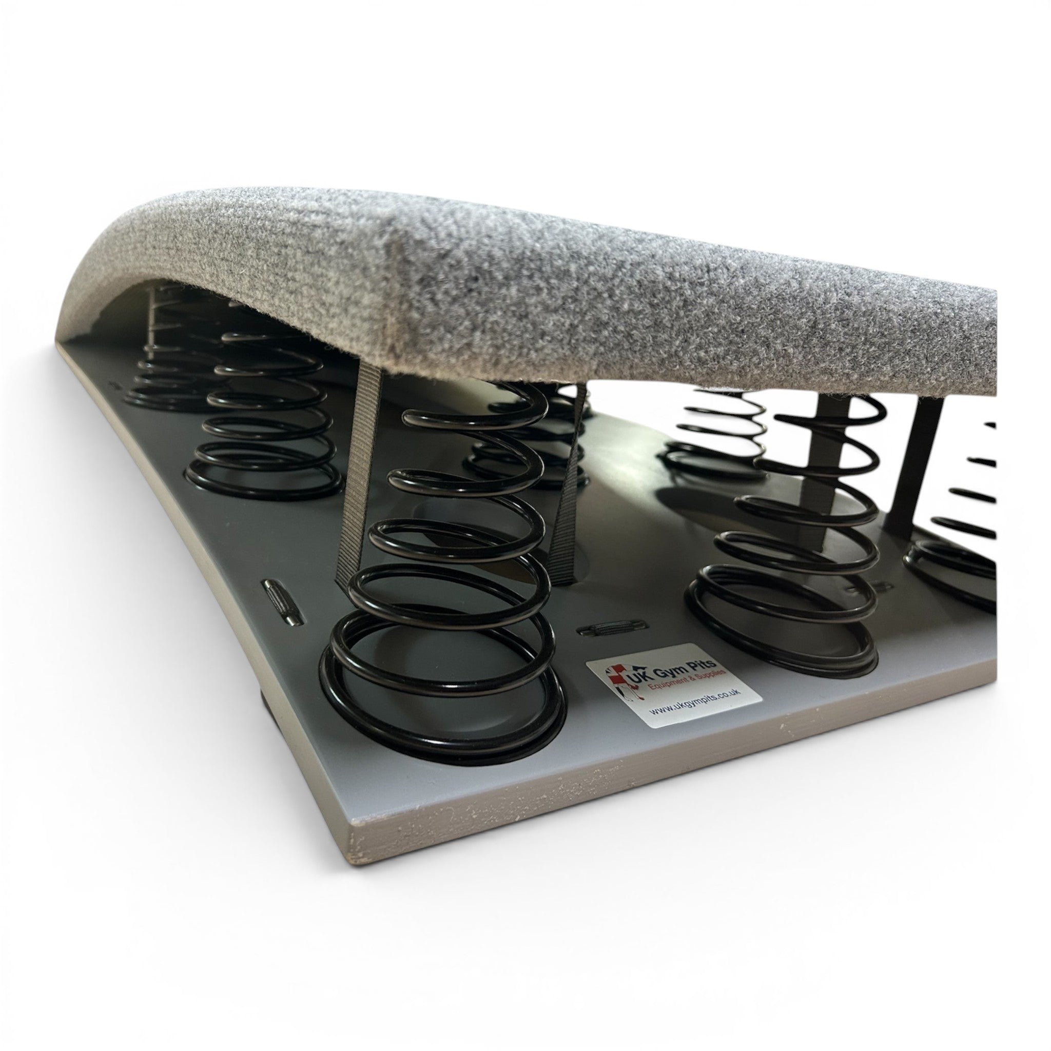 UK Gym Pits FIG approved gymnastics springboard with grey carpeted surface and visible black tapered steel springs