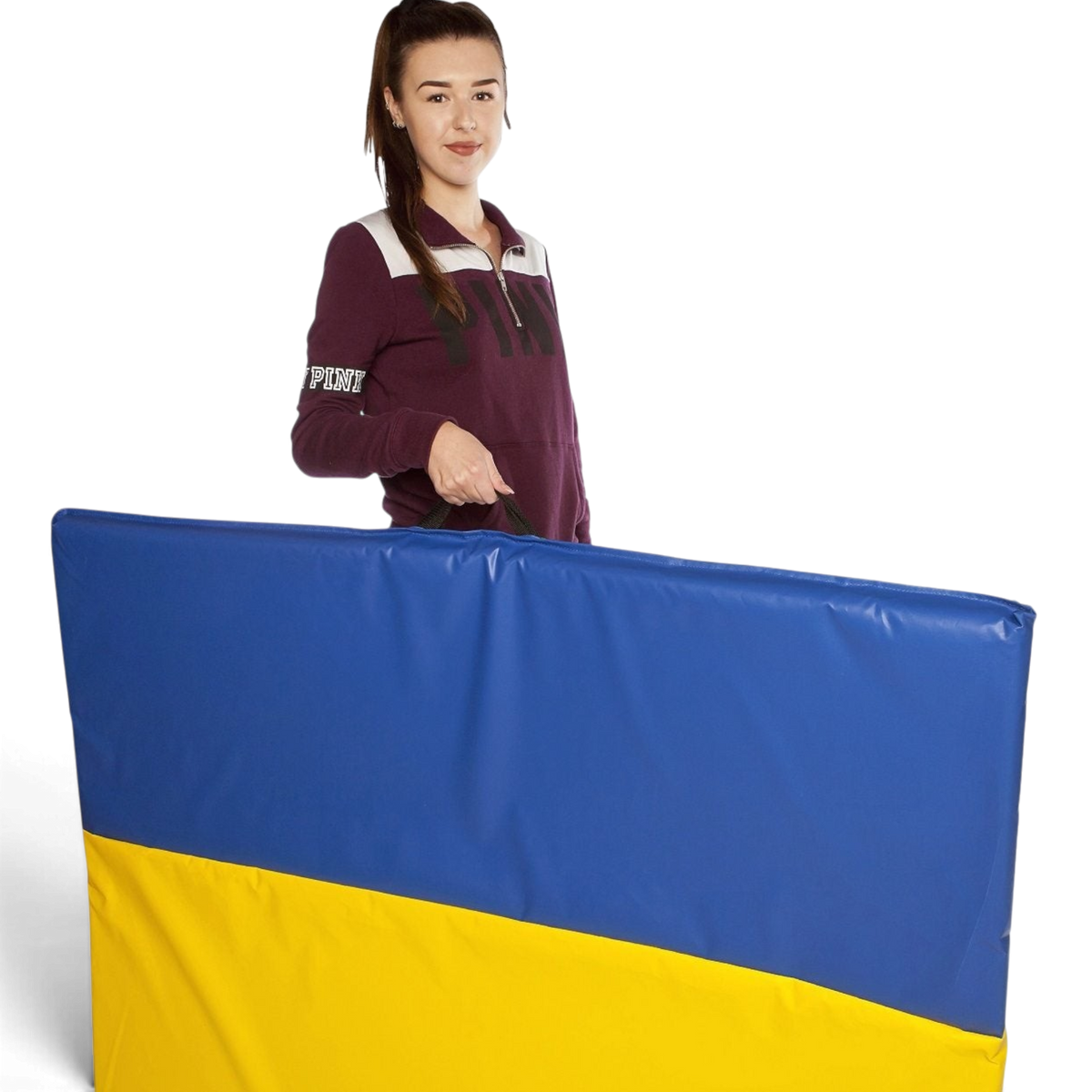 UK Gym Pits folding tumble mat in blue and yellow PVC with a carry handle, held by a woman in a studio setting.